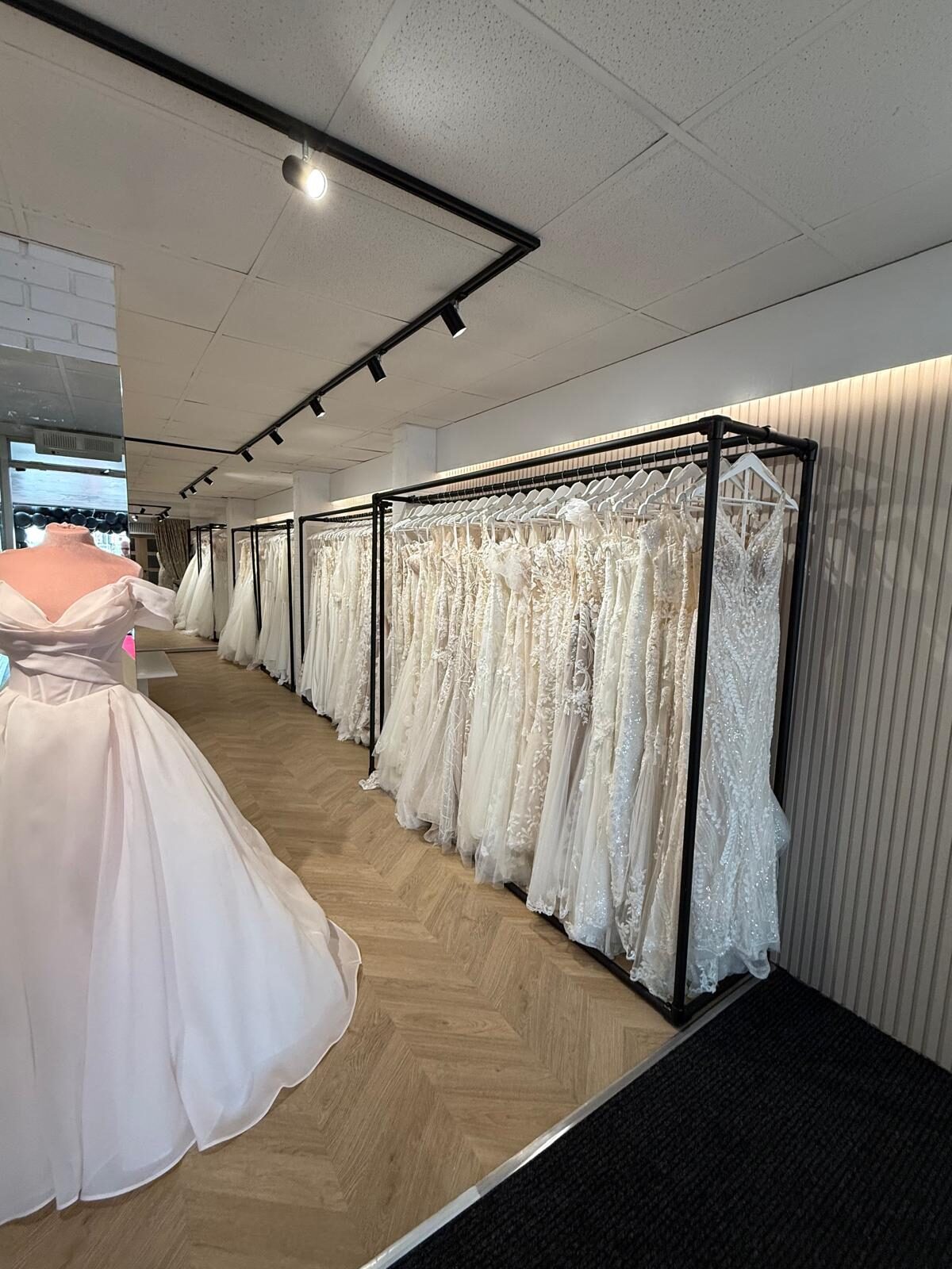 A displayed wedding gown beside rails of dresses in the boutique